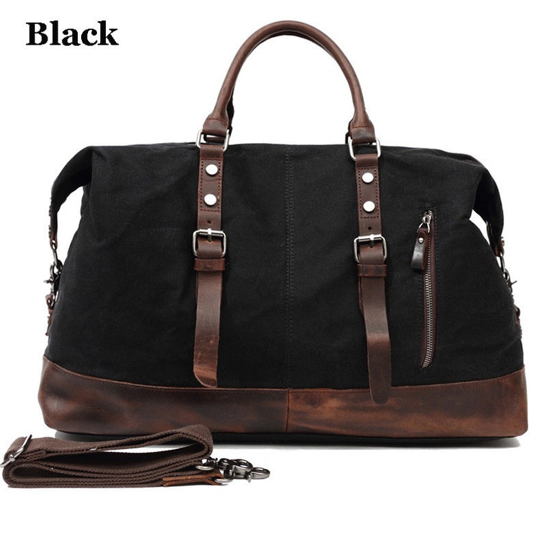 May include: Black duffel bag with brown leather accents. The bag features a top handle, shoulder strap, and a zippered side pocket. The bottom and straps are made of brown leather, and the bag has the word "Black" in the top left corner.