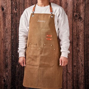 May include: A brown canvas apron with leather straps and a large pocket. The apron has the name "Jimmy" embroidered on the front.