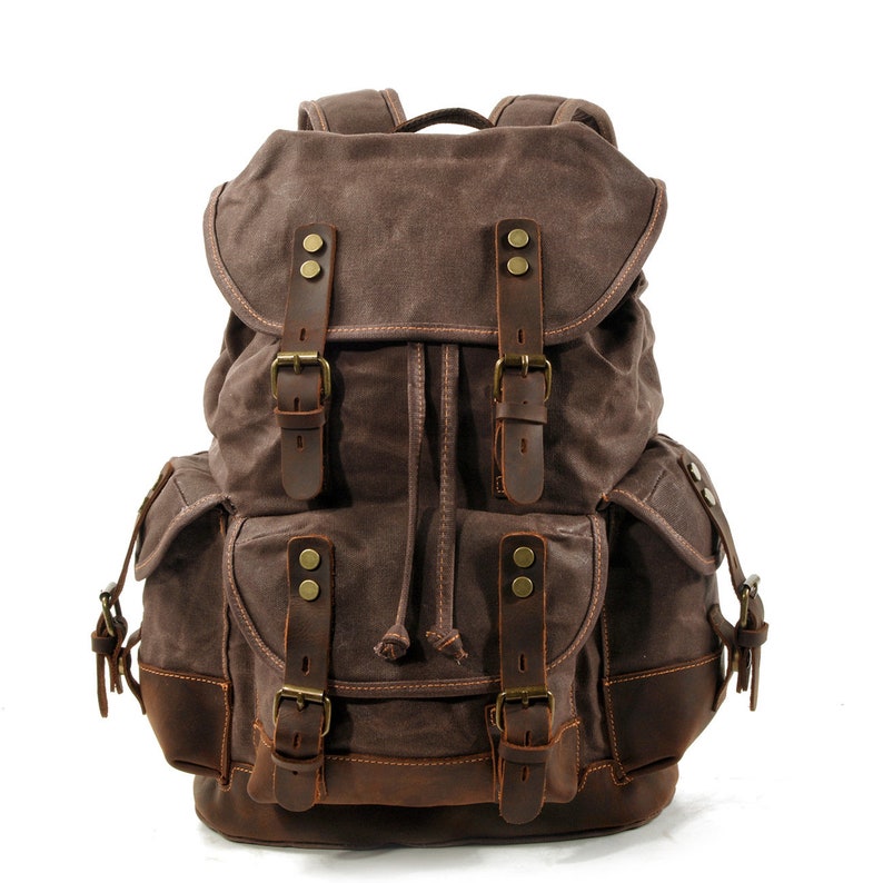 Puede incluir: Una mochila de lona marr&oacute;n con detalles de cuero y varios bolsillos. La mochila tiene un cierre de cord&oacute;n y correas ajustables.