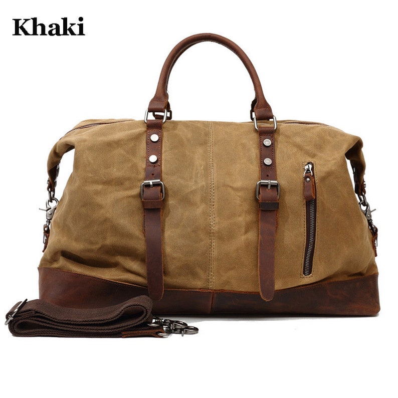 May include: Khaki canvas duffel bag with brown leather accents. Features include a top handle, shoulder strap, and a side zipper pocket. The bag has a rectangular shape and metal hardware.