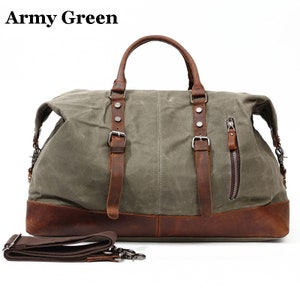 May include: Army green duffel bag with brown leather accents. The bag features a top handle, shoulder strap, and a side zipper pocket. The bag has a brown leather base and straps with silver buckles.
