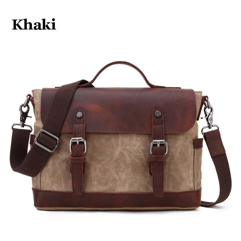 May include: Khaki messenger bag with a brown leather flap and accents. The bag has a top handle and a shoulder strap. The bag has two buckles and a small pocket on the side. The word "Khaki" is in the top left corner.