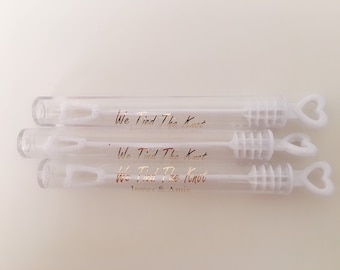 May include: Three clear plastic bubble wands with heart-shaped handles. Each wand has a gold inscription that reads "We Tied The Knot" and the bottom wand also includes the names "James & Amie".