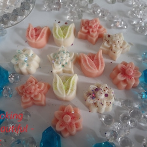 May include: Assortment of wax melts in various flower shapes, including tulips, stars, and daisies. The melts are in shades of pink, white, and green, with some featuring glitter accents.