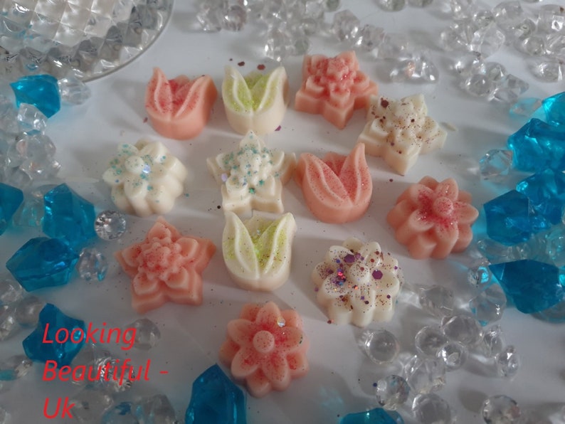May include: Assortment of wax melts in various flower shapes, including tulips, stars, and daisies. The melts are in shades of pink, white, and green, with some featuring glitter accents.