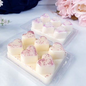 May include: A clear plastic tray filled with heart-shaped wax melts. The melts are white with pink glitter embedded in them.