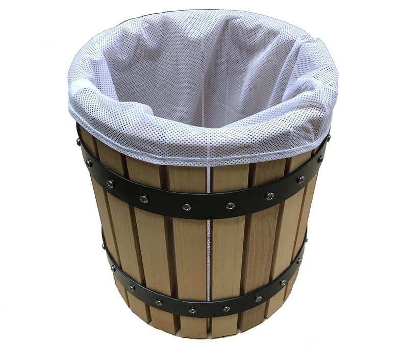 May include: A wooden barrel with vertical wooden staves and black metal bands. A white mesh bag lines the interior. The barrel is designed for pressing fruits or vegetables, likely for making juice or cider.
