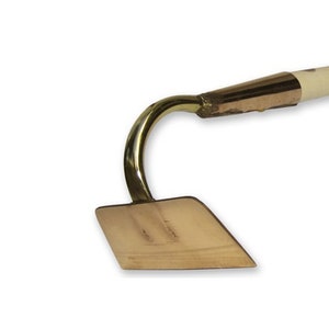 Könnte beinhalten: Eine Gartenhandhacke aus Messing mit einem Holzstiel. Die Hacke hat einen gebogenen Hals und eine flache, rautenförmige Klinge.
