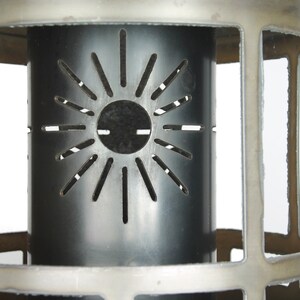 Könnte beinhalten: Eine silberne Metall-Laterne mit einem ausgeschnittenen Sonnenmotiv in der Mitte. Die Laterne hat eine zylindrische Form und ist aus Metall.