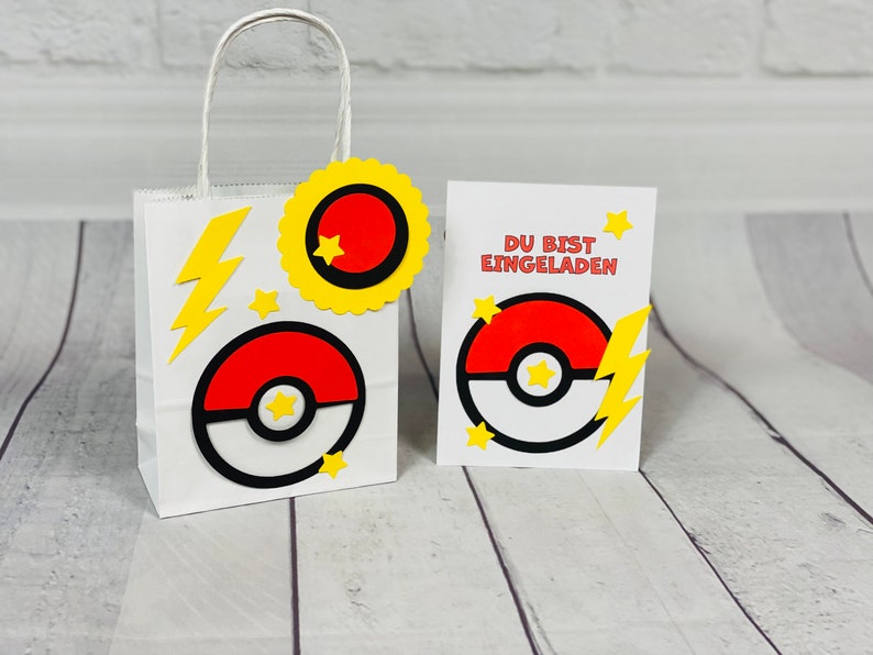 Puede incluir: Una bolsa de regalo de papel blanco con un dise&ntilde;o de Pokeball amarillo y rojo. La bolsa tiene un rayo amarillo y estrellas. Una tarjeta blanca con un dise&ntilde;o de Pokeball amarillo y rojo y el texto "DU BIST EINGELADEN" en rojo.