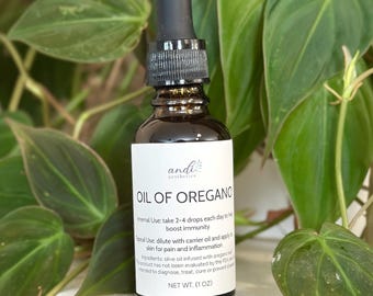 May include: A brown glass bottle of Oil of Oregano with a black dropper, set against a backdrop of green leaves. The label reads "andi aesthetics" and details for internal and topical use. Net weight is 1 oz.
