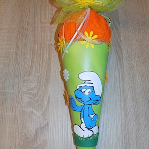 Könnte beinhalten: Eine grüne und orangefarbene Schultüte mit einem Schlumpf-Charakter. Der Kegel ist mit gelben und weißen Blumen und einer grünen Schleife verziert. Die Spitze ist mit orangefarbenem Seidenpapier gefüllt.