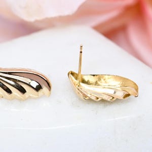 Puede incluir: Un par de pendientes de bot&oacute;n de oro en forma de concha. Los pendientes tienen un dise&ntilde;o texturizado y acanalado.