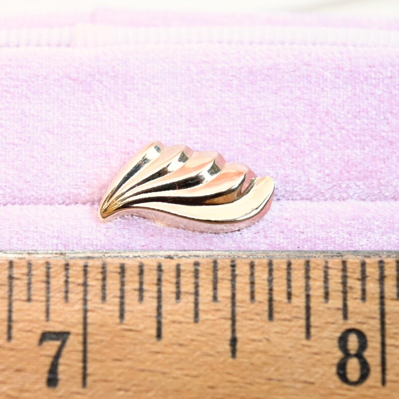 Puede incluir: Un pendiente de metal dorado con un dise&ntilde;o en forma de abanico. El pendiente mide aproximadamente 2,5 cm de largo.