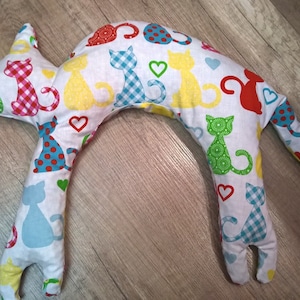 Könnte beinhalten: Ein weißes, U-förmiges Nackenstützkissen mit einem bunten Katzenmuster. Das Kissen ist mit kleinen, bunten Katzen und Herzen gefüllt.