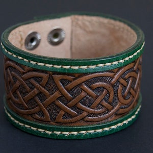 May include: A brown leather bracelet with a Celtic knot design and green stitching.