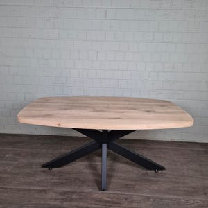 Op de afbeelding: Een eettafel van licht hout met een rechthoekig blad en een zwarte, X-vormige basis.