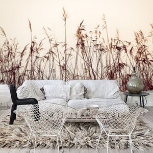 May include: A white couch with two white wire chairs in front of it. The couch and chairs are in a room with a white rug and a white wall with a brown and white grass print wallpaper.