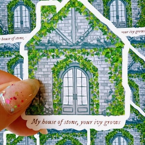 May include: A sticker featuring a house illustration with a stone facade and green ivy. The house has arched windows and a door. Text on the sticker reads, "My house of stone, your ivy grows."