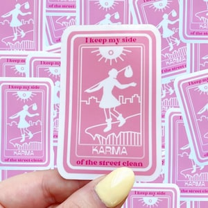 May include: Pink sticker with a white silhouette of a person holding a bag walking on a street with buildings. The sticker says "I keep my side of the street clean" and "KARMA" in pink letters.