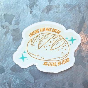 May include: A white sticker with a cartoon illustration of a loaf of bread. The text "LOAFING HIM WAS BREAD" arches above the bread, and "BR-EEEAD, BR-EEEAD" is below. Teal starbursts accent the design.