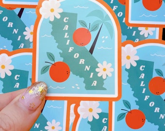 May include: A set of colorful stickers featuring a stylized outline of the state of California with the words "California" and "California fornia" written vertically. The stickers feature a palm tree, orange slices, and white daisies.