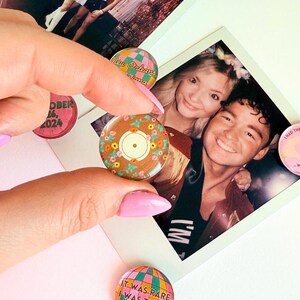 Pode incluir: Uma cole&ccedil;&atilde;o de quatro pinos redondos de vidro coloridos com v&aacute;rios designs. Um pino apresenta um disco com acentos florais, outro tem um globo com o texto "It was rare, I was there", outro tem um design xadrez com o texto "New Orleans, Diana", e o &uacute;ltimo pino tem um mostrador de rel&oacute;gio com o texto "October 16, 2024".