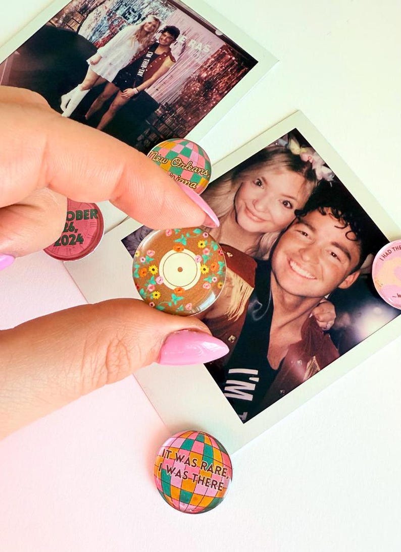 Pode incluir: Uma cole&ccedil;&atilde;o de quatro pinos redondos de vidro coloridos com v&aacute;rios designs. Um pino apresenta um disco com acentos florais, outro tem um globo com o texto "It was rare, I was there", outro tem um design xadrez com o texto "New Orleans, Diana", e o &uacute;ltimo pino tem um mostrador de rel&oacute;gio com o texto "October 16, 2024".