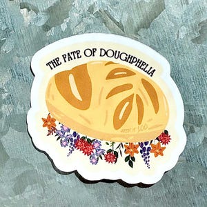 May include: A sticker featuring a cartoon loaf of bread with the text "THE FATE OF DOUGHPHELIA." The bread is light brown with darker brown details. The sticker is decorated with colorful flowers.