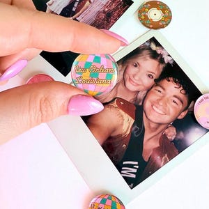 Pode incluir: Dois pinos redondos de vidro coloridos com um design de bola de discoteca. Um pino diz "Nova Orleans Louisiana" e o outro diz "Era raro, eu estava l&aacute;."