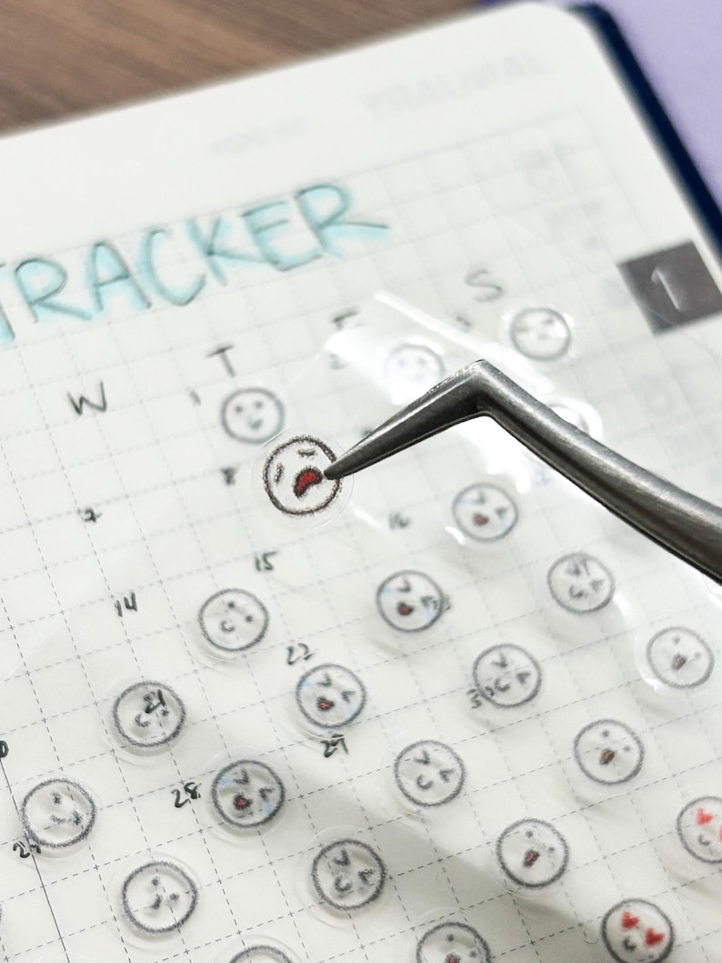 May include: A clear sheet of stickers with various facial expressions. The stickers are arranged in a grid pattern on a white surface. The stickers are designed to be used as a mood tracker.