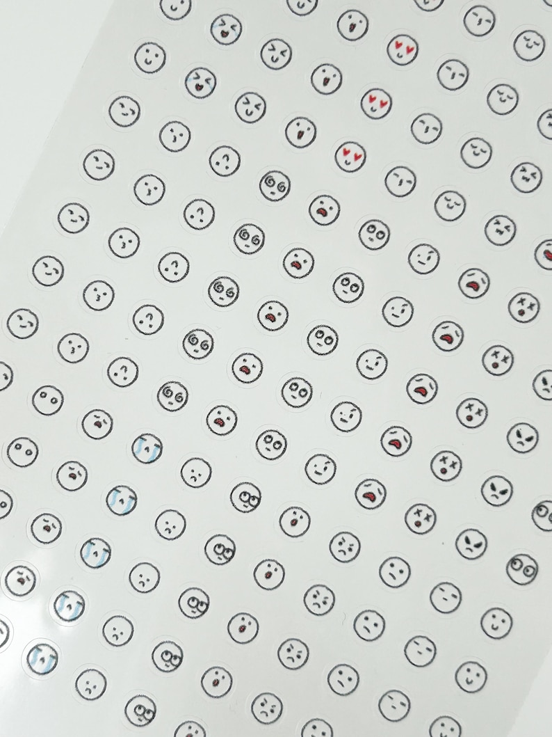 May include: A sheet of white sticker paper with a variety of black and white cartoon faces. The faces have different expressions, including happy, sad, surprised, and confused.
