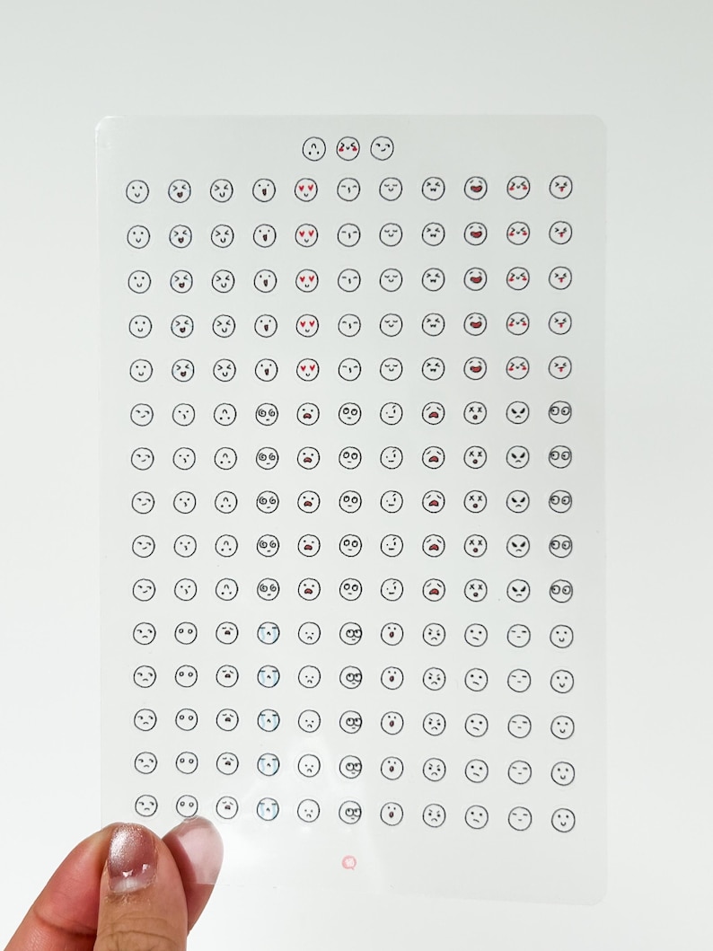 May include: A sheet of clear stickers with a variety of black and white emoji faces. The emojis include happy, sad, surprised, and angry faces.