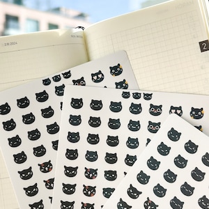 May include: A sheet of black cat stickers with different facial expressions. The stickers are on a white background and are arranged in rows. The stickers are perfect for adding a touch of whimsy to planners, journals, and other paper goods.