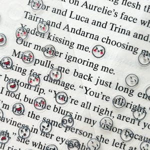 May include: A close-up of a page of text with several small, clear stickers with different facial expressions. The stickers are scattered across the page, some overlapping. The text on the page is blurry, but the stickers are in focus.