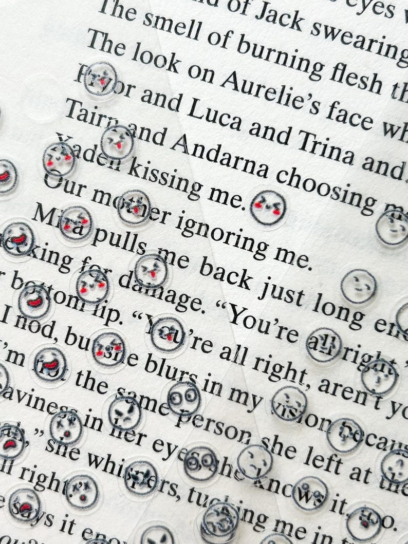 May include: A close-up of a page of text with several small, clear stickers with different facial expressions. The stickers are scattered across the page, some overlapping. The text on the page is blurry, but the stickers are in focus.