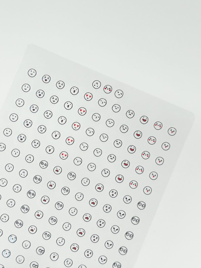 May include: A sheet of clear sticker paper with a variety of black and white emoji faces. The emojis include smiling, frowning, surprised, and hearts for eyes.