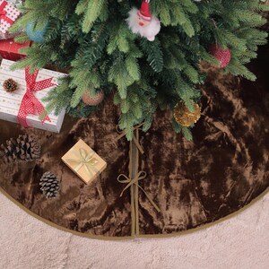 Puede incluir: Un &aacute;rbol de Navidad decorado con una falda de &aacute;rbol de terciopelo marr&oacute;n. Varios regalos envueltos en rojo, blanco y dorado se colocan alrededor del &aacute;rbol. Tambi&eacute;n se ven pi&ntilde;as y una caja de flores.