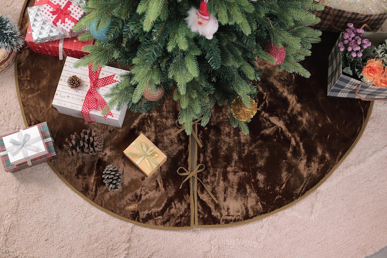 Puede incluir: Un &aacute;rbol de Navidad decorado con una falda de &aacute;rbol de terciopelo marr&oacute;n. Varios regalos envueltos en rojo, blanco y dorado se colocan alrededor del &aacute;rbol. Tambi&eacute;n se ven pi&ntilde;as y una caja de flores.