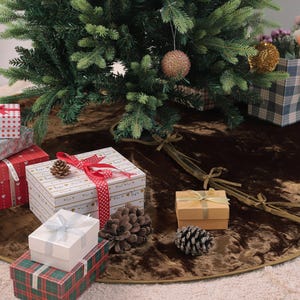 Puede incluir: Un &aacute;rbol de Navidad decorado con una falda de &aacute;rbol marr&oacute;n. Varias cajas de regalo envueltas en varios tama&ntilde;os y patrones est&aacute;n dispuestas alrededor de la base del &aacute;rbol. Tambi&eacute;n hay una bolsa de regalo a cuadros llena de flores.