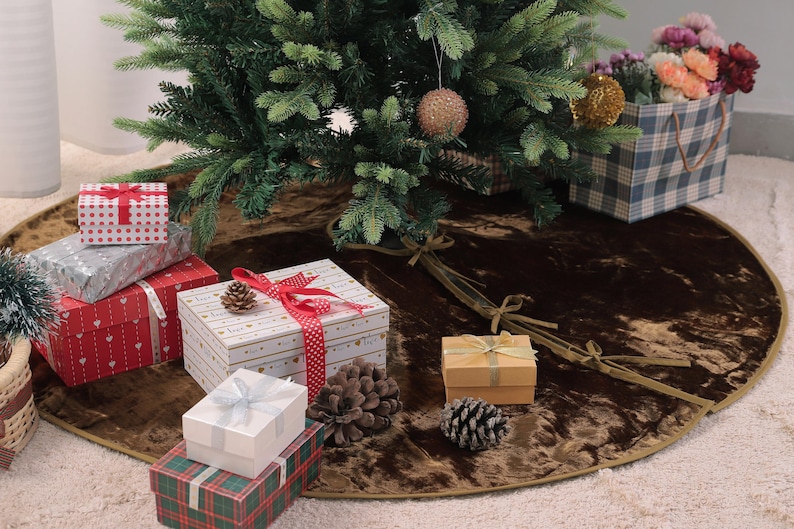 Puede incluir: Un &aacute;rbol de Navidad decorado con una falda de &aacute;rbol marr&oacute;n. Varias cajas de regalo envueltas en varios tama&ntilde;os y patrones est&aacute;n dispuestas alrededor de la base del &aacute;rbol. Tambi&eacute;n hay una bolsa de regalo a cuadros llena de flores.