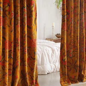 May include: Mustard-coloured curtains with a detailed floral pattern in red, orange, and black. The curtains are made of a thick fabric and are hanging in front of a white bed. The floral design is intricate and covers the entire surface of the curtains.