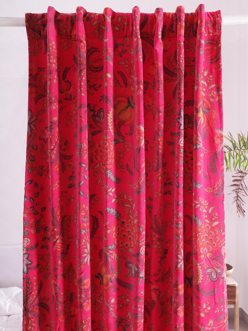 K&ouml;nnte beinhalten: Hellrosa Vorh&auml;nge mit floralem Muster. Die Vorh&auml;nge weisen ein detailliertes Design mit Rot-, Orange- und Graut&ouml;nen auf. Der Stoff ist oben gerafft, wodurch vertikale Falten entstehen. Die Vorh&auml;nge h&auml;ngen vor einer wei&szlig;en Wand.