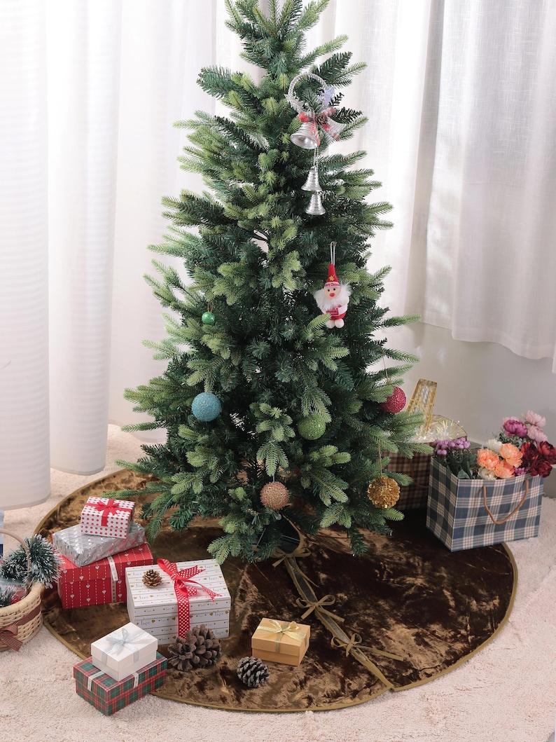 Puede incluir: Un &aacute;rbol de Navidad artificial decorado con adornos y una figura de Pap&aacute; Noel. El &aacute;rbol se encuentra sobre una falda de &aacute;rbol marr&oacute;n, rodeado de regalos envueltos y pi&ntilde;as. Tambi&eacute;n hay una bolsa de regalo a cuadros y flores.