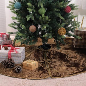 Puede incluir: Un &aacute;rbol de Navidad decorado con adornos coloridos se alza sobre una falda de &aacute;rbol de terciopelo marr&oacute;n. Regalos envueltos en varios tama&ntilde;os y patrones, junto con pi&ntilde;as, est&aacute;n dispuestos alrededor de la base, creando una escena festiva.
