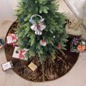 Puede incluir: Un &aacute;rbol de Navidad decorado con adornos y una decoraci&oacute;n de campana plateada. Los regalos envueltos en papel de colores y cintas est&aacute;n dispuestos alrededor del &aacute;rbol sobre una falda de &aacute;rbol marr&oacute;n. Cestas de flores y golosinas completan la escena festiva.