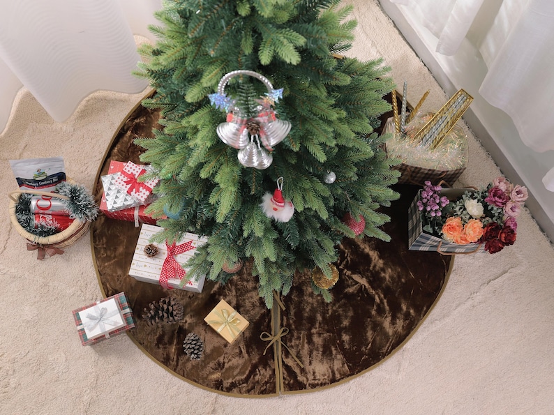 Puede incluir: Un &aacute;rbol de Navidad decorado con adornos y una decoraci&oacute;n de campana plateada. Los regalos envueltos en papel de colores y cintas est&aacute;n dispuestos alrededor del &aacute;rbol sobre una falda de &aacute;rbol marr&oacute;n. Cestas de flores y golosinas completan la escena festiva.