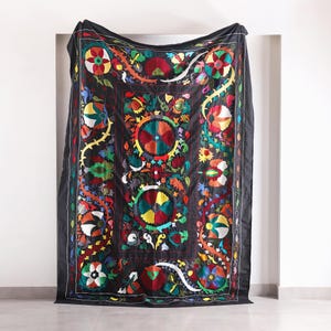 Può includere: Arazzo da parete in tessuto nero con motivi floreali e geometrici ricamati colorati.