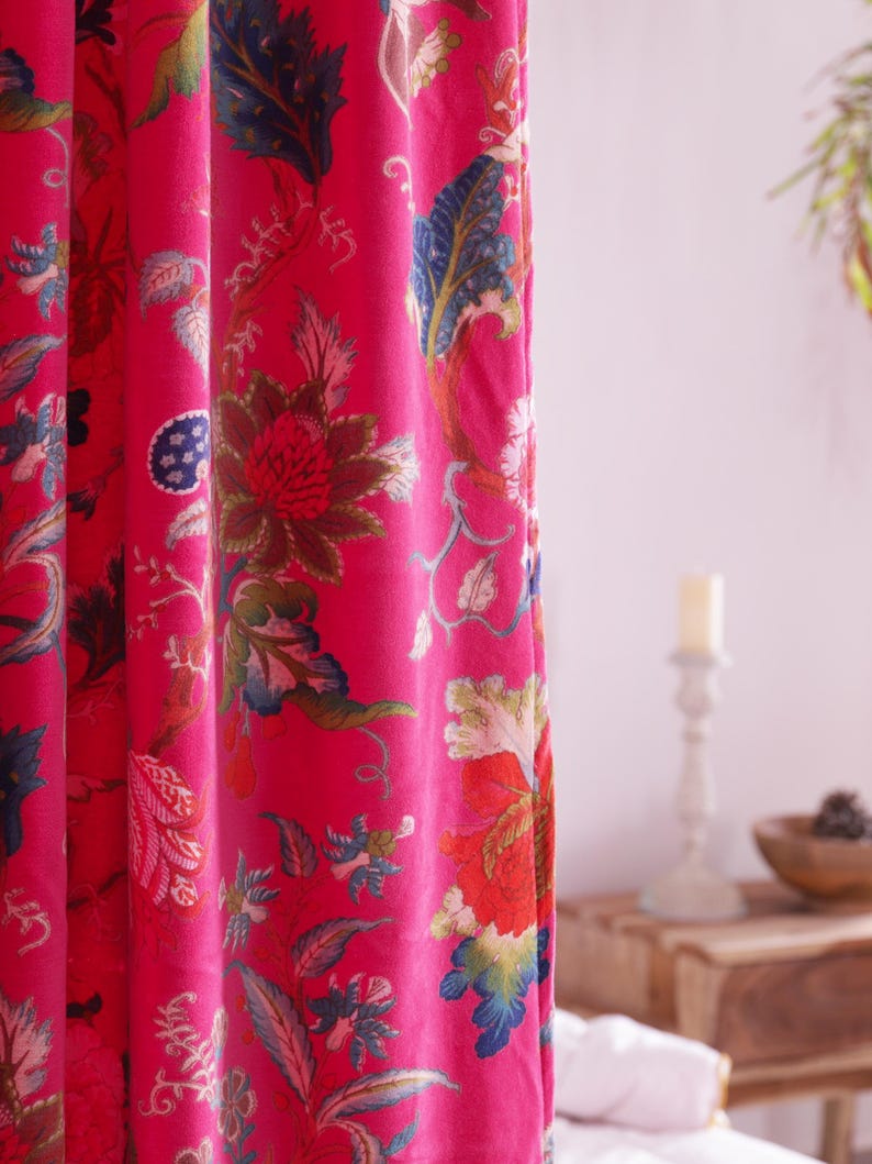 K&ouml;nnte beinhalten: Leuchtend pinkfarbener Vorhang mit gro&szlig;em Blumenmuster. Der Stoff zeigt ein botanisches Design mit roten, blauen, gr&uuml;nen und cremefarbenen Blumen und Bl&auml;ttern. Der Vorhang besteht aus einem weichen, flie&szlig;enden Material und ist teilweise zugezogen.