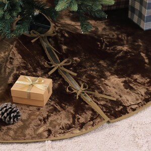 Puede incluir: Una falda de &aacute;rbol de Navidad de terciopelo marr&oacute;n con ribete dorado. La falda est&aacute; decorada con peque&ntilde;os regalos, pi&ntilde;as y una cinta. La falda est&aacute; dise&ntilde;ada para colocarse alrededor de la base de un &aacute;rbol de Navidad.